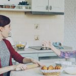 Young mother and cute daughter cooking together talking in the kitchen on weekend. Little funny girl clapping hands with flour and laughing. Family, food, home and people concept